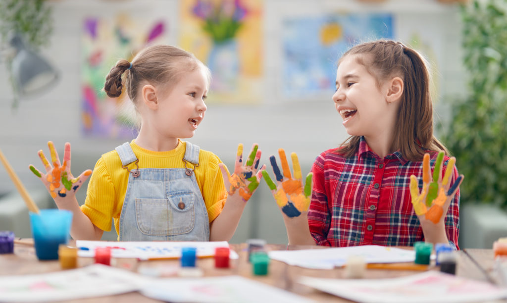 smiling-kids-with-painted-hands-and-papers-and-paints-on-the-table-in-the-art-room